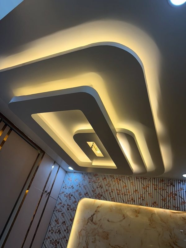 Completed bedroom interior with curved layered false ceiling, warm cove lighting and backlit marble-look panel